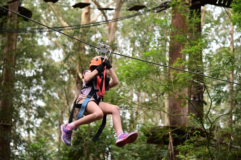 a young girl zip lines on a flying fox through nature